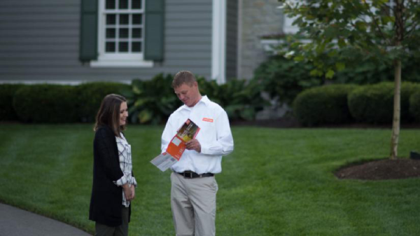 A man shows brochures to a woman outside a house