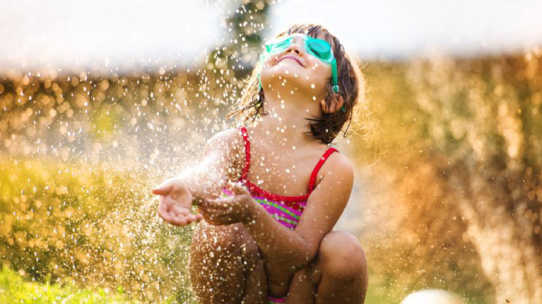 A young girl in a bathing suit joyfully splashes water.